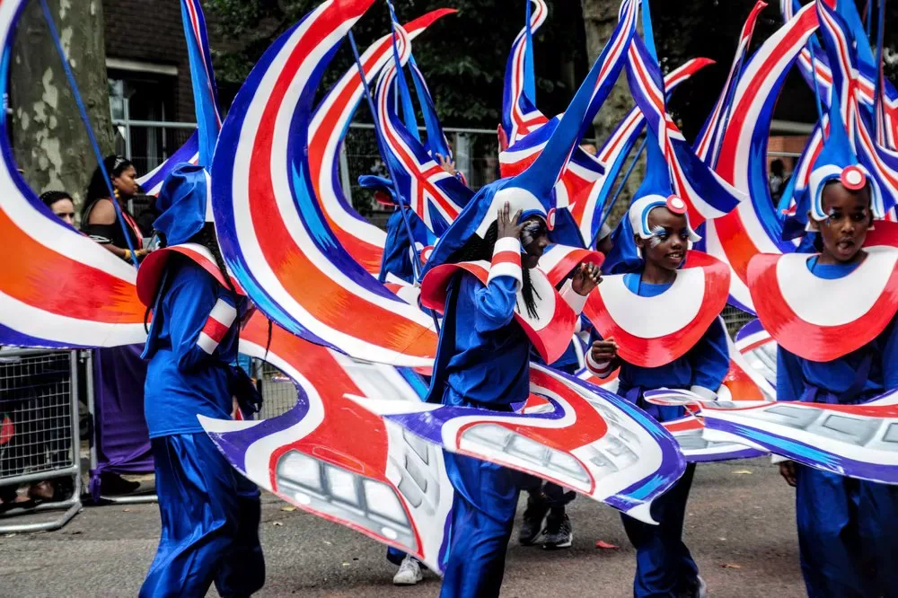 Children in blue, red and white costumes taking part in the Notting Hill Carnival parade