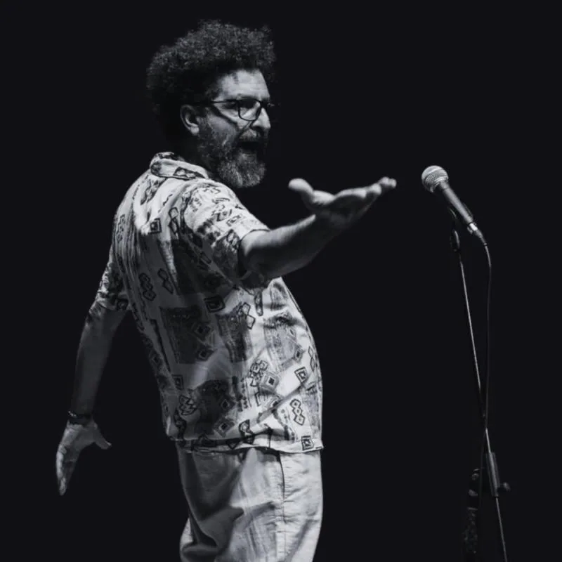 Comedian Hanna Shammas gesturing at a microphone in a black-and-white performance photograph