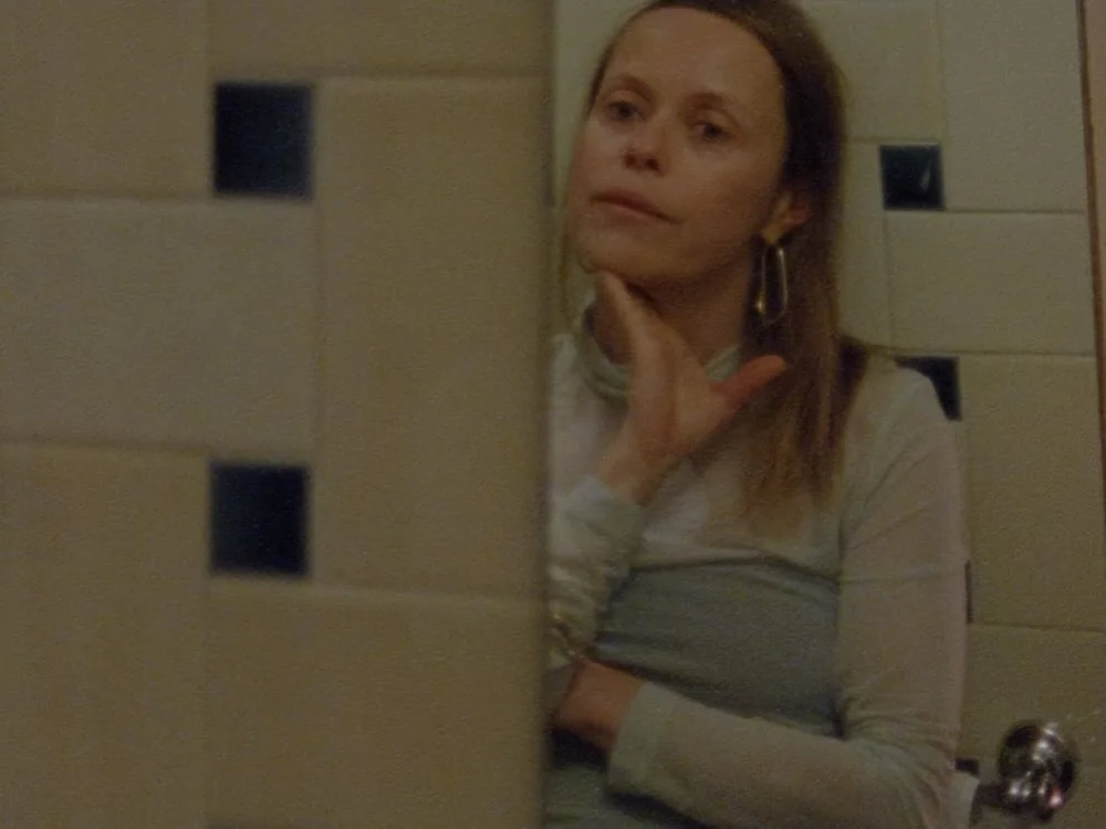A woman pauses in a tiled room in a film still from Beatrice Gibson’s At Night