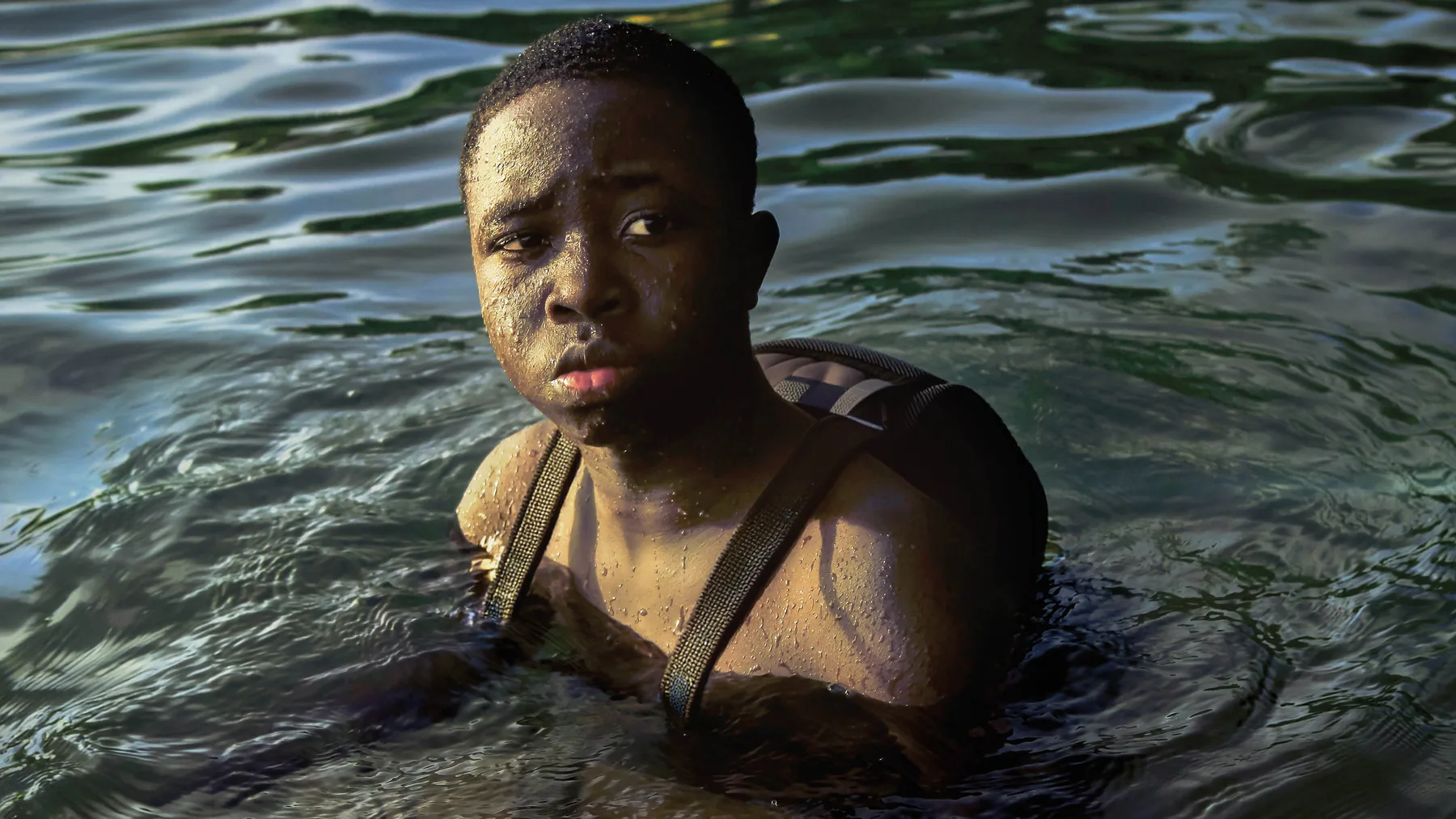 A young Black boy half-submerged in water in the production image for Our Eyes Looking for God